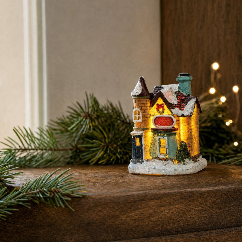 Small illuminated Christmas village house on warm wood beside fresh fir branches