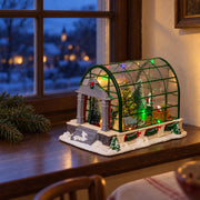 Multicolored LED Christmas greenhouse on a walnut window ledge at dusk