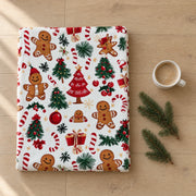 Folded gingerbread print Christmas throw on an oak floor beside fir sprigs and a white cup