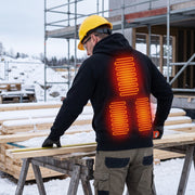 Worker wearing the black heated hoodie on a winter construction site, with the supplier's three back heating zones illustrated as a schematic red overlay.