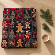 Folded tartan gingerbread Christmas throw on an oak floor beside fir sprigs and a white cup