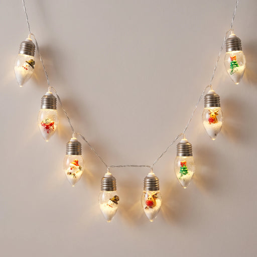 Snow globe Christmas bulb string lights hanging in a warm white arc against a pale wall