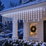 Icicle curtain lights glowing cool white under the porch eaves of a snowy cottage at dusk