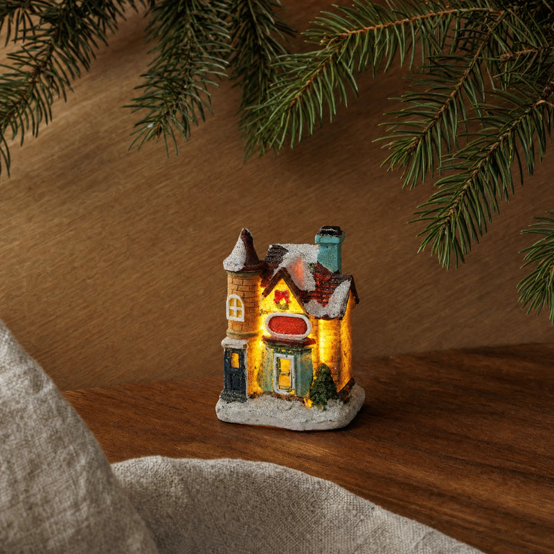 Small Christmas village house in a warm wood tabletop arrangement with fir branches