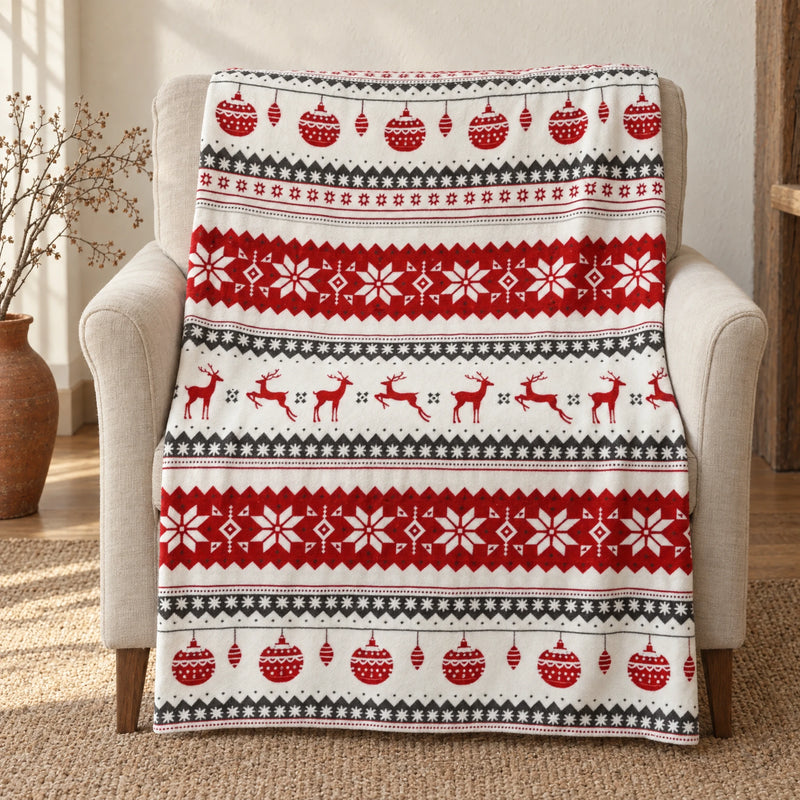 Fair isle Christmas throw blanket with a red and grey reindeer print, draped over a linen armchair