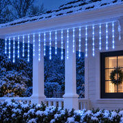 Icicle curtain lights glowing blue under the porch eaves of a snowy cottage at dusk