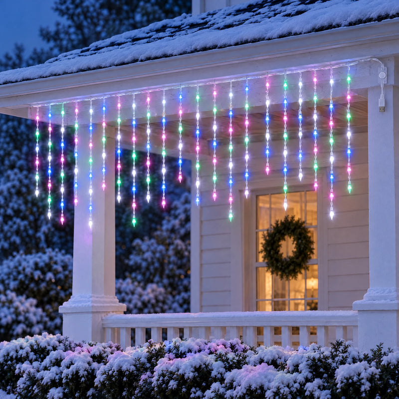 Icicle curtain lights glowing in mixed pink, blue, green and white under the porch eaves of a snowy cottage at dusk