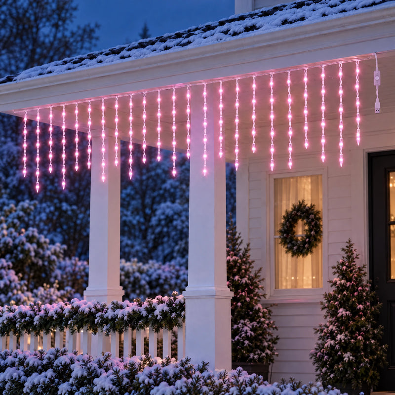 Icicle curtain lights glowing soft pink under the porch eaves of a snowy cottage at dusk