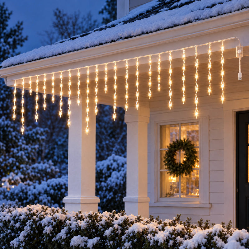 Icicle curtain lights glowing warm gold under the porch eaves of a snowy cottage at dusk