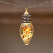 Close-up of a clear glass Christmas bulb with a silver screw cap holding a Santa figurine in artificial snow