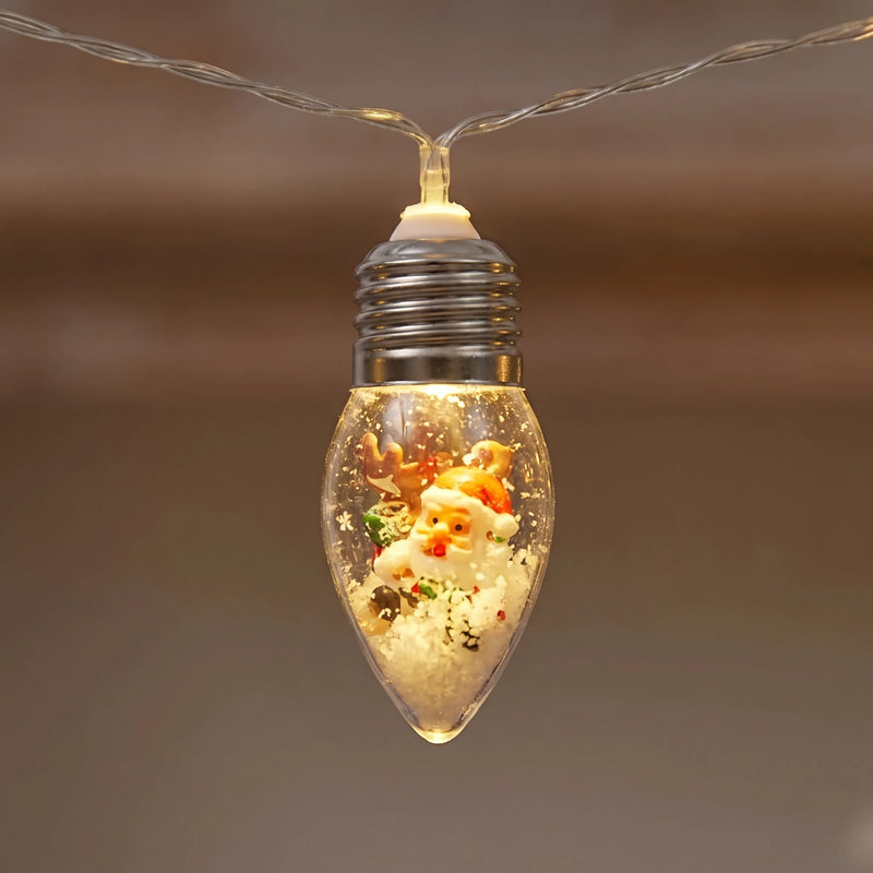 Close-up of a clear glass Christmas bulb with a silver screw cap holding a Santa figurine in artificial snow