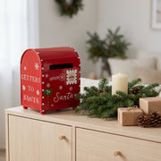 Red Christmas mailbox on a wooden sideboard with fir branches, a candle and wrapped gifts