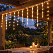 Icicle curtain lights glowing warm gold from a wooden pergola above an outdoor table at dusk