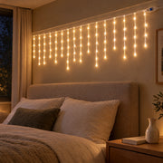 Icicle curtain lights lit above a linen headboard in a bedroom