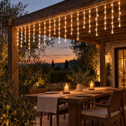 Icicle curtain lights hanging from a pergola above an outdoor table at dusk