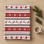 Folded fair isle Christmas throw on an oak floor beside fir sprigs and a white cup