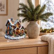 Flat acrylic Christmas snowhouse decoration on a light oak sideboard with fir branches and snow outside