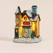 Illuminated snow-covered resin Christmas village house on a pale cream background
