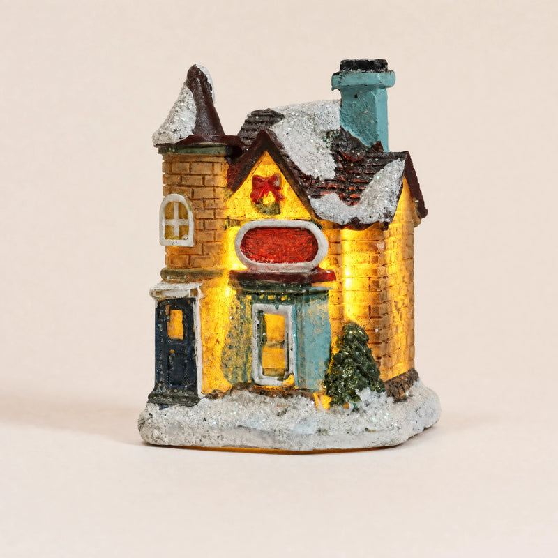 Illuminated snow-covered resin Christmas village house on a pale cream background