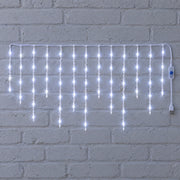 White icicle curtain light hung against a white brick wall