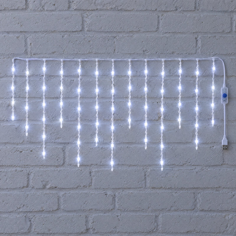 White icicle curtain light hung against a white brick wall