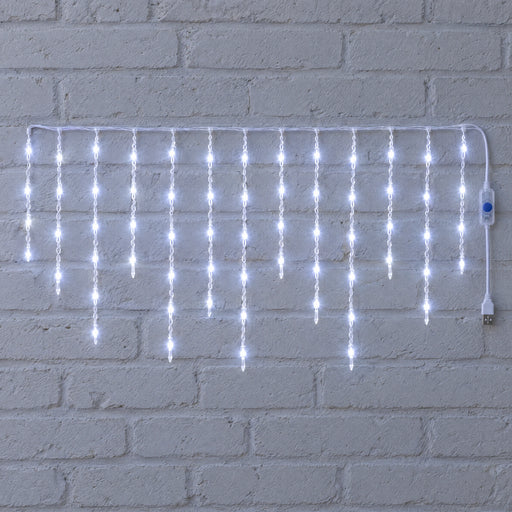 White icicle curtain light hung against a white brick wall