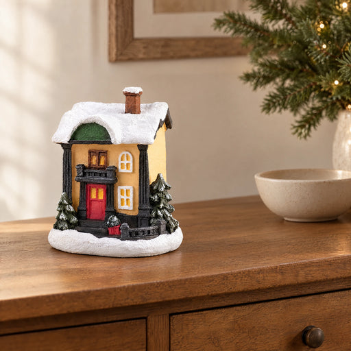 Resin Christmas village miniature on a wooden entryway console with fir greenery