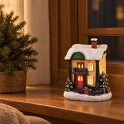 Illuminated resin Christmas village house on an indoor wooden window ledge at dusk