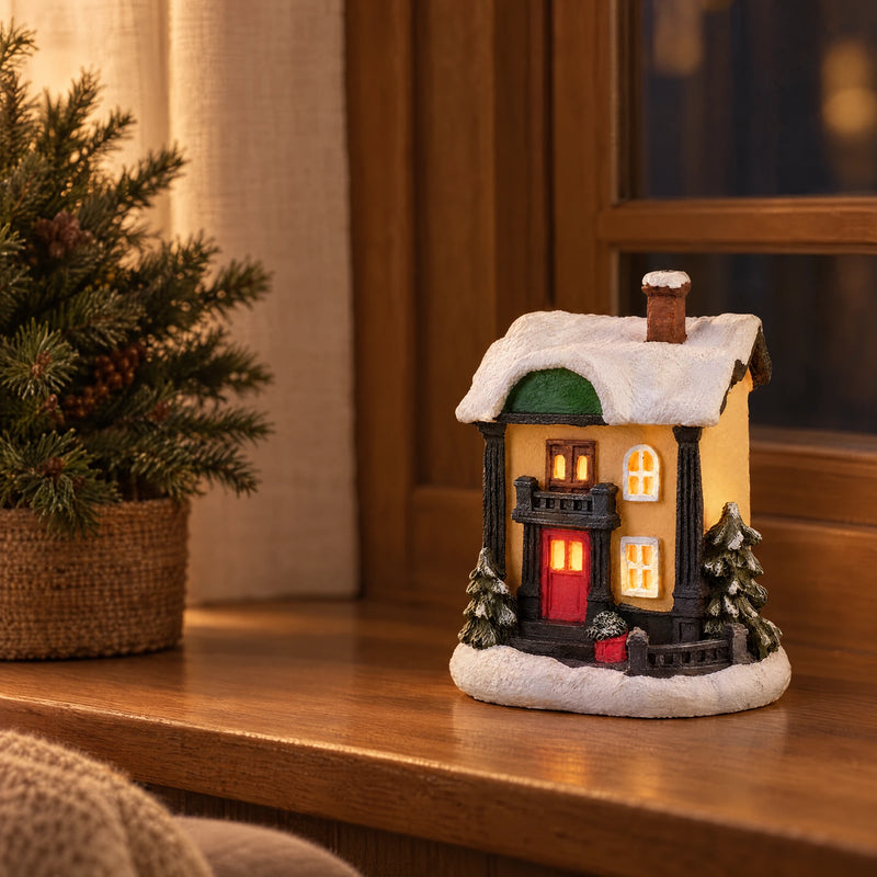 Illuminated resin Christmas village house on an indoor wooden window ledge at dusk