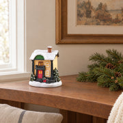 Resin Christmas village miniature on a wooden shelf with linen and natural fir greenery