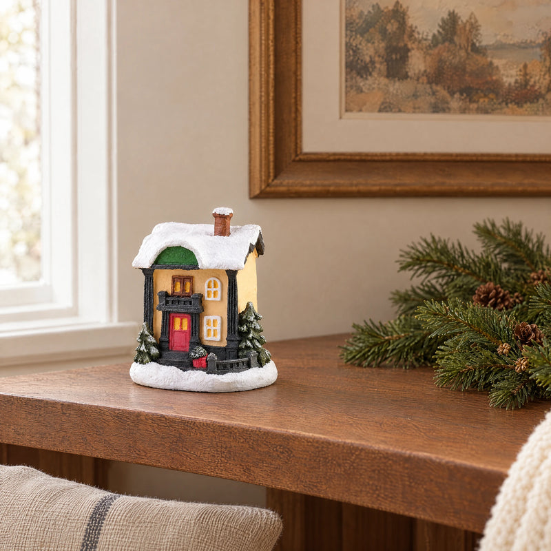 Resin Christmas village miniature on a wooden shelf with linen and natural fir greenery