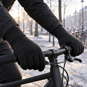 Black winter gloves worn on hands gripping a bicycle handlebar on a cold morning